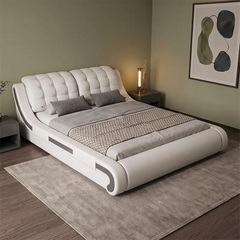 A modern white upholstered bed with a tufted headboard and curved footboard, styled in a minimalist bedroom with gray bedding, a gray rug, and a lit bedside lamp.