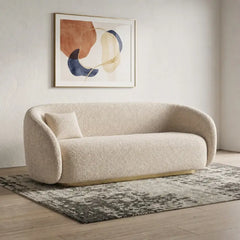 Curved sofa with brushed gold base and rounded supportive arms, front three-quarter view